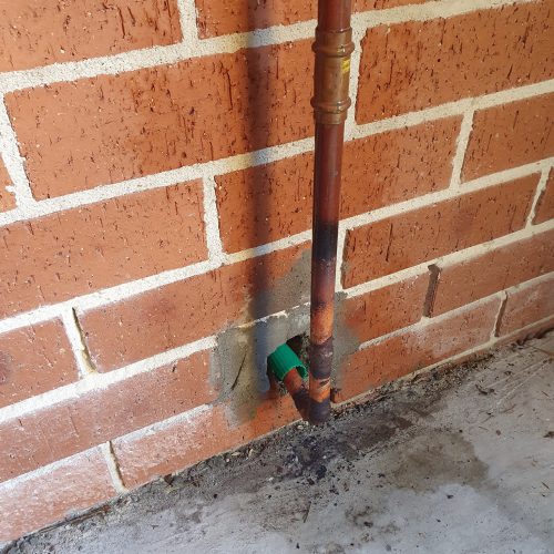 Replacement copper gas line with protective sleeve through brickwork